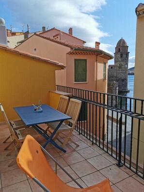 A balcony with a table and chairs, overlooking a body of water and a historic tower. - Casa Finote - COLLIOURE (COLLIOURE)