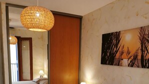 A bedroom with a bed, a hanging light fixture, a nightstand with a lamp, and a wall-mounted painting.