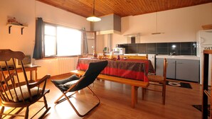 Une pièce chaleureuse avec un plafond en bois, une table à manger avec des chaises, un coin cuisine et une fenêtre avec des rideaux.
