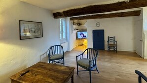 A spacious room with a wooden table and two chairs, a television in the background, and a blue door.