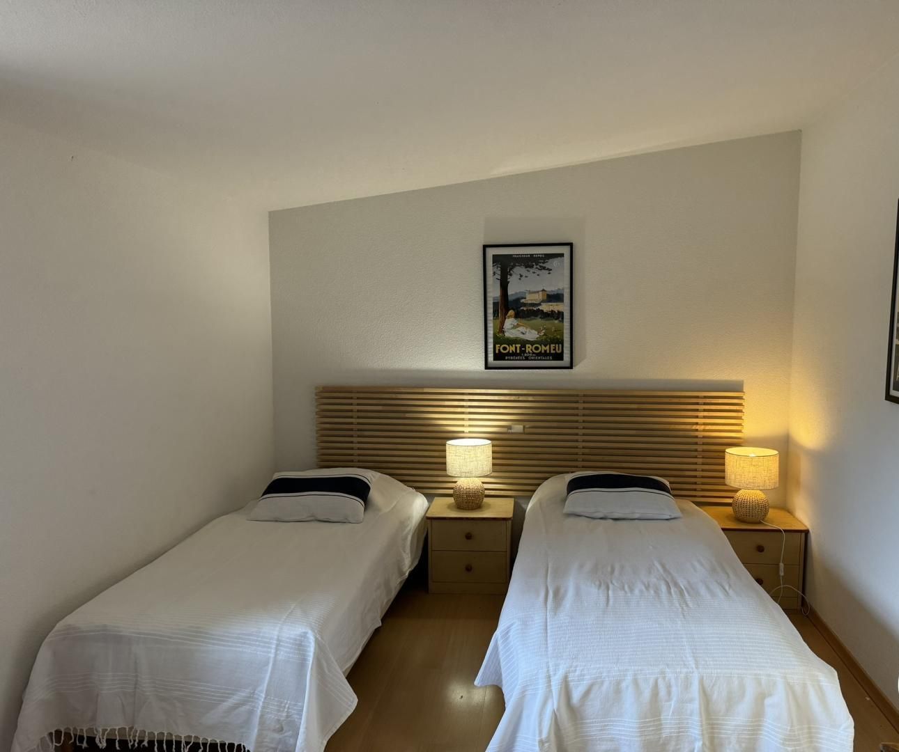 A hotel room with two single beds, wooden headboards, bedside lamps, and two framed posters on the wall.
