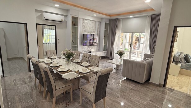 A modern dining area with a marble floor, a long dining table set for six, and a comfortable sofa in the background.