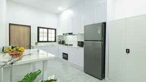 A modern kitchen with white cabinets, a stainless steel refrigerator, a marble countertop, and a window with blinds.