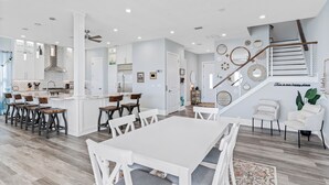 Une cuisine moderne avec des meubles blancs, un îlot central et un coin repas comprenant des chaises et une table, le tout dans des tons blancs.