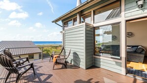 Una casa moderna con una terraza que da al océano, con un gran ventanal corredera y una zona de estar acogedora con sofá y sillones.