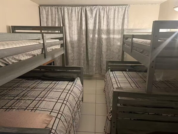 A dormitory room with bunk beds, a patterned bedspread, and a curtain.