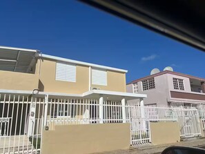 A residential building with a beige facade, white window shutters, and a white fence.