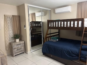 Un dormitorio con una cama litera, un armario, una mesita con una planta y un equipo de aire acondicionado.
