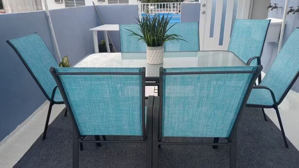 Une terrasse avec une table en verre entourée de quatre chaises, une plante en pot et une petite table.