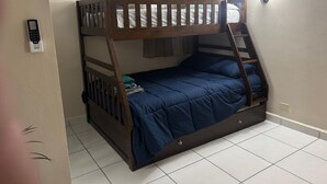 Un lit superposé avec une structure en bois et une literie bleue, un climatiseur blanc et un rideau à la fenêtre.