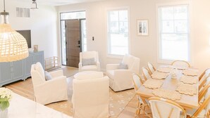Un salón espacioso con comedor, mobiliario de colores claros y ventanas amplias.