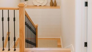 Una escalera con barandilla de madera y balaustres negros, que lleva a un rellano con pared blanca y un arreglo floral decorativo.