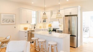 Una cocina moderna con armarios blancos, un refrigerador de acero inoxidable y una isla central con taburetes.