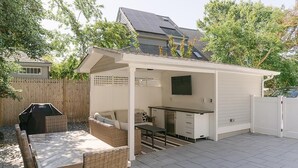 Un patio cubierto con mesa y sillas, una parrilla y una pequeña cocina con pileta y armarios.
