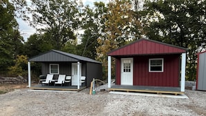 Deux petits chalets dotés d’un espace extérieur pour s’asseoir, l’un avec une véranda et l’autre avec une porte.