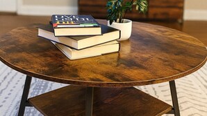 Ein runder Couchtisch aus Holz mit einer Büchtel Bücher und einer Topfpflanze.