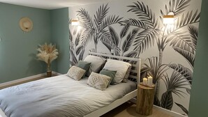 Un dormitori amb un llit, una tauleta de nit, una làmpada penjada a la paret i una pared decorada amb un dibuix de fulles tropicals.