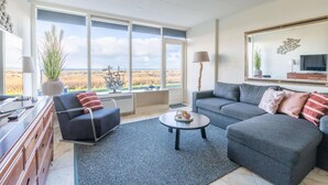 Un salon moderne avec une grande fenêtre, un canapé, une table basse et un téléviseur.