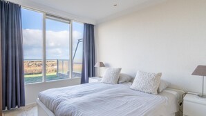 Une chambre à coucher avec un grand lit, deux tables de chevet, une lampe et une vue sur l’extérieur.