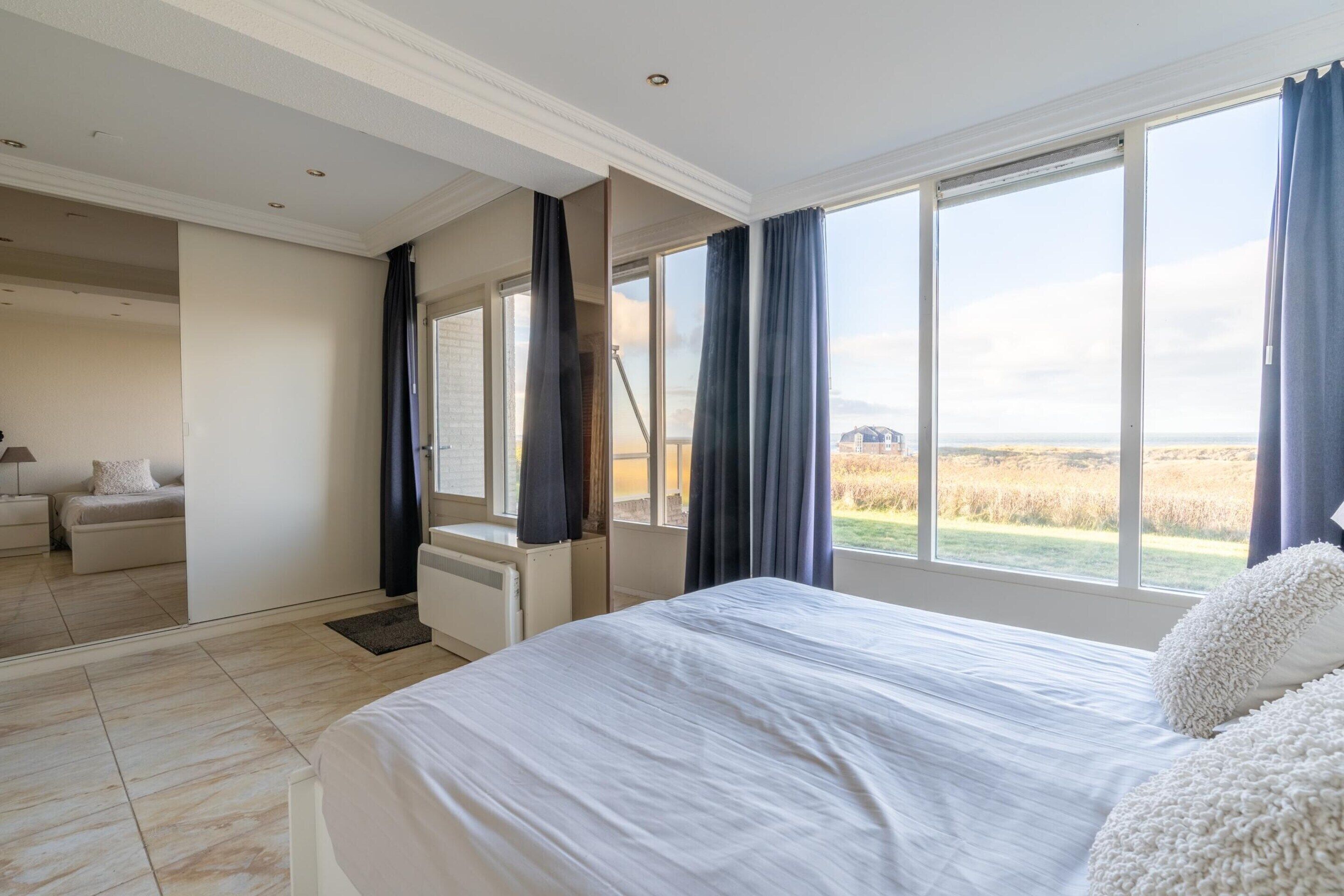 A bedroom with a large bed, a view of a field, and a separate living area with a sofa and lamp.