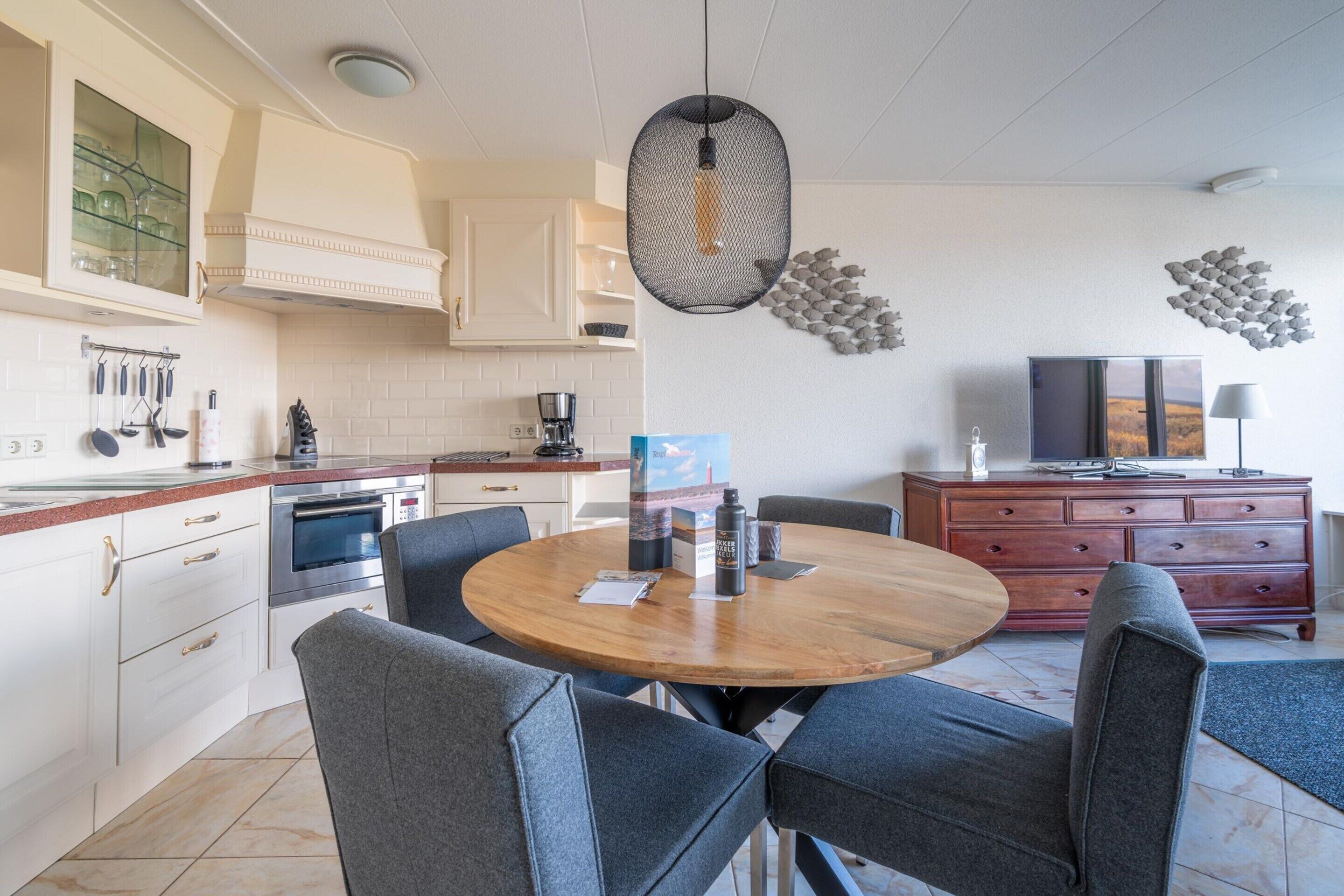 A modern kitchen with white cabinets, a round wooden table, and grey upholstered chairs.