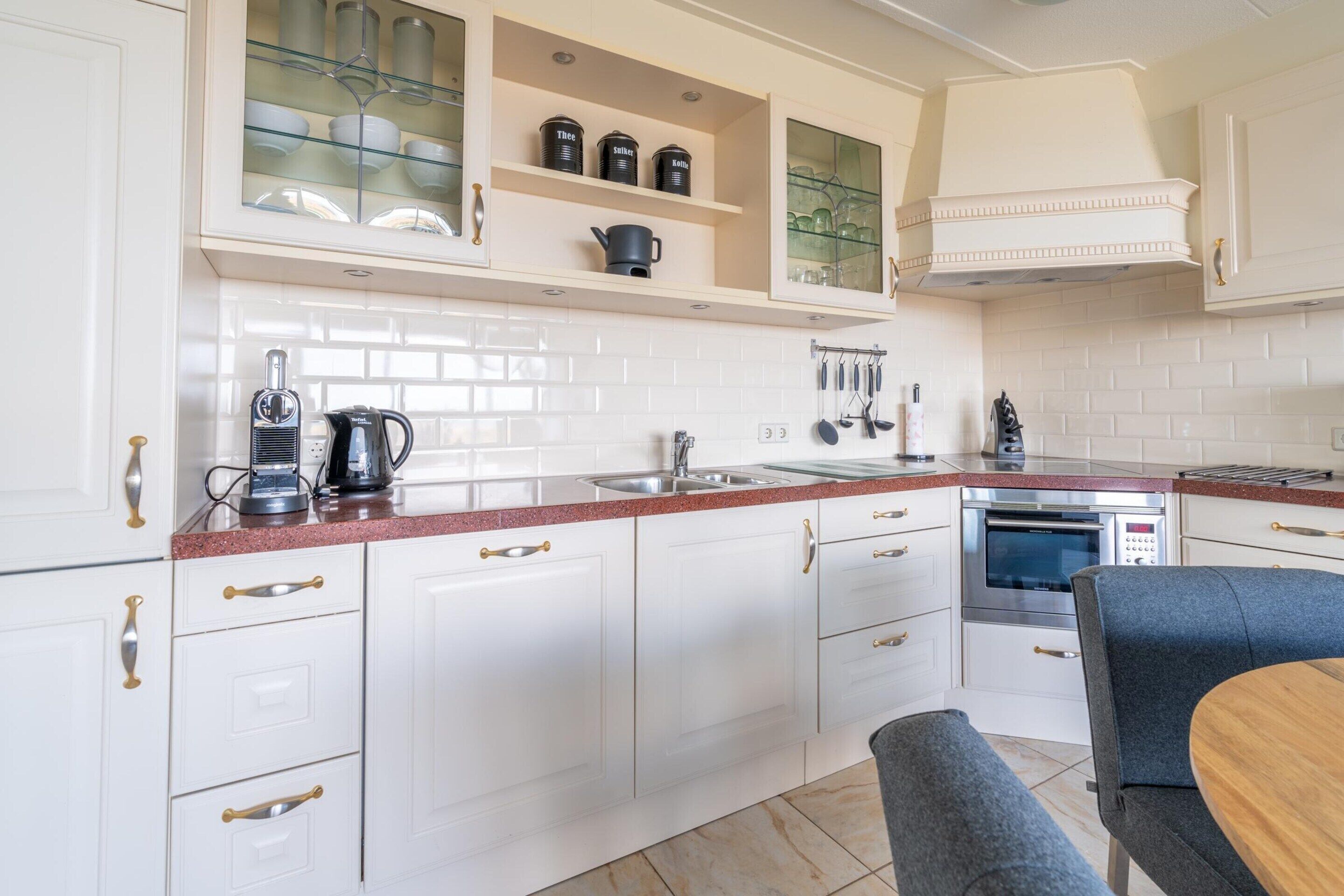 Una cucina moderna con mobili bianchi, un piano di lavoro in granito, un forno integrato e un'area pranzo con tavolo e due sedie.