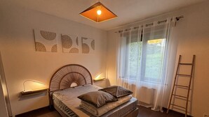 Ein Schlafzimmer mit einem Bett, Nachttischlampen, einem Fenster mit Vorhängen, einer Leiter und Wandbildern.