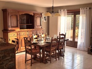 Un coin repas avec une table et des chaises en bois, un meuble encastré en bois, et une vue à travers une porte vitrée.