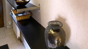 Ein Flur mit schwarzer Arbeitsplatte, einem gewebten Korb, einer Vase und Holzregalen mit Spiegeln.