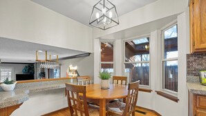 A dining area with a wooden table and chairs, a chandelier, and a view of the outdoors through large windows. - Spacious Family Retreat: Central/Hot Tub/Pool Table/Fire Pit/Kids Toys/3KingBeds (Arvada)