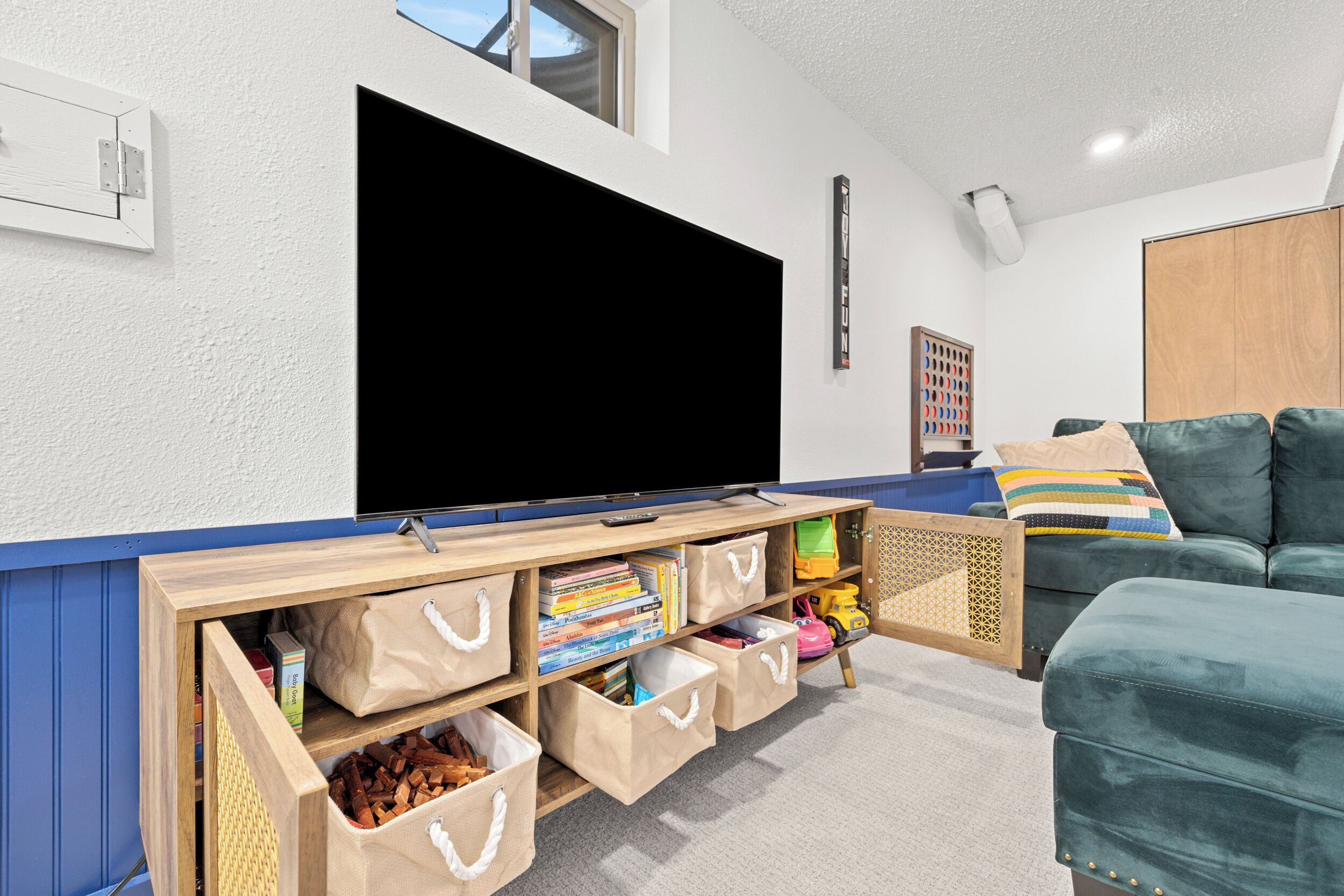 A living room with a large flat-screen TV, wooden storage units, a green sofa, and a wooden cabinet.