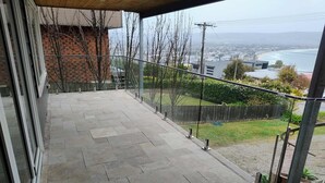 Uma varanda com ladrilhos de pedra, vista para uma cidade costeira e um muro de tijolos.