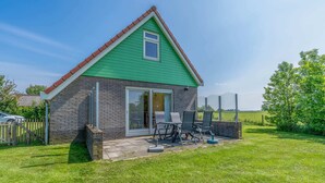 Une petite maison avec un toit végétalisé et des murs en briques, une porte-fenêtre coulissante et une terrasse aménagée avec du mobilier d’extérieur.