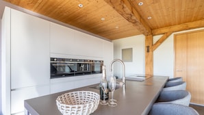 A modern kitchen with white cabinets, a built-in oven, and a large island with a basket and glasses. - Modern 6-person Villa With Private Hot Tub - Near Beach & Nature (De Koog)