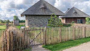 A rustic building with a stone facade and a thatched roof, surrounded by a wooden fence and a gravel path. - Modern 6-person Villa With Private Hot Tub - Near Beach & Nature (De Koog)