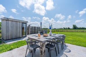 Ein Essbereich im Freien mit einem Tisch, gedeckt für sechs Personen, umgeben von Stühlen, einer kleinen Holzkonstruktion und blauem Himmel.