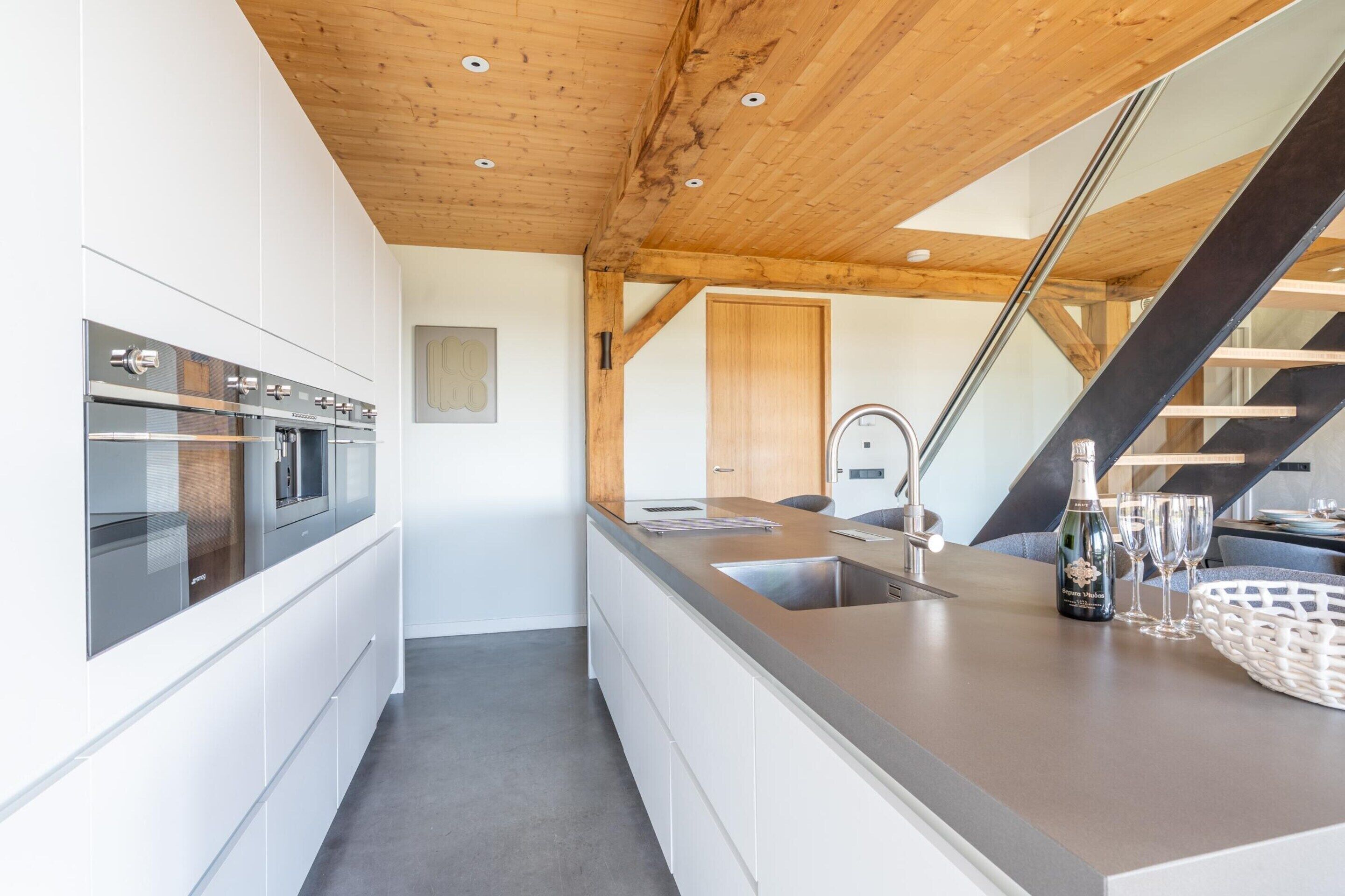 Een moderne keuken met roestvrijstalen apparatuur, een houten plafond en een groot eiland met een spoelbak en wijnglazen.