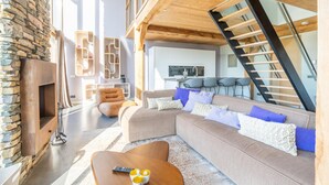 A modern living room with a stone fireplace, a large sofa, and a wooden staircase. - Modern 6-person Villa With Private Hot Tub - Near Beach & Nature (De Koog)