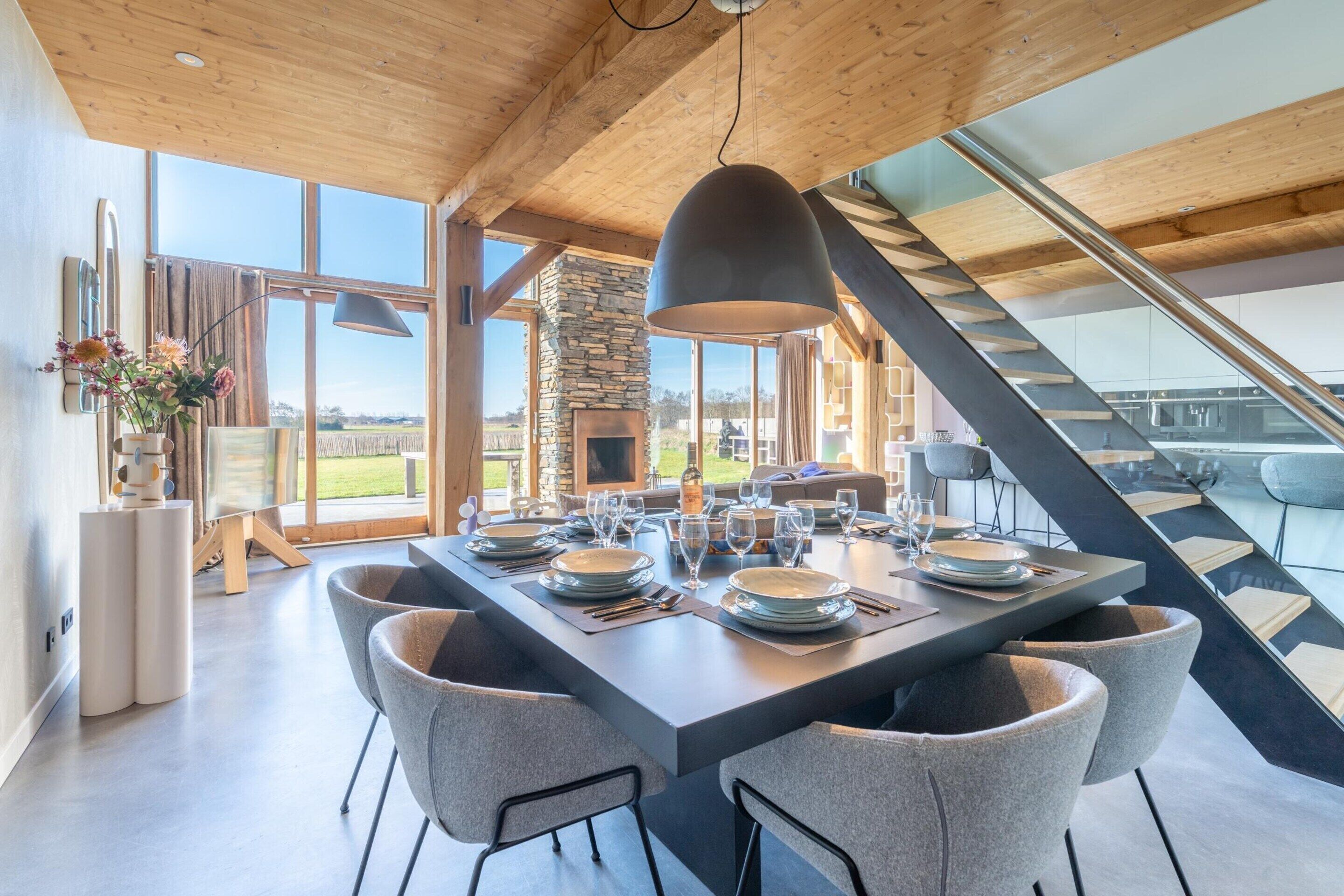 Uma sala de jantar moderna com uma mesa grande posta para seis pessoas, uma lareira de pedra e vista para o exterior.