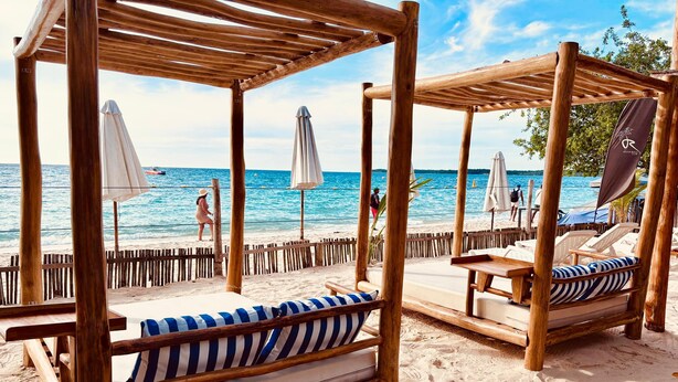 A beachside wooden structure with two beds, each with a striped cushion and a white umbrella. - Rocha Beach Club (Cartagena)