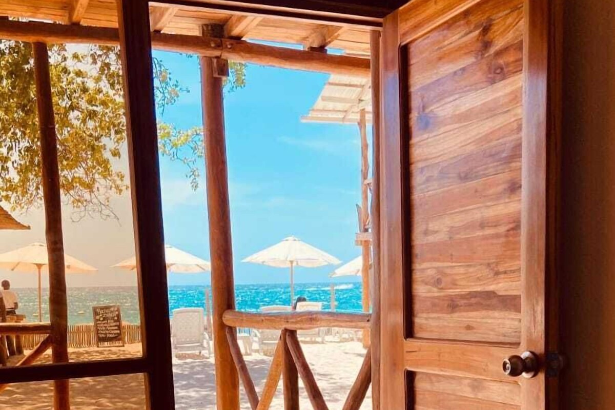 A wooden door leading to a beach area with umbrellas and a view of the ocean.