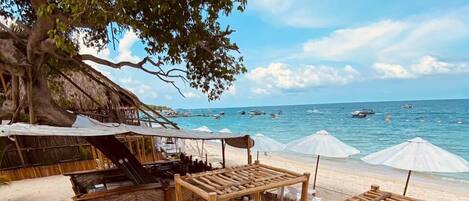 Une plage avec des chaises longues en bois et une structure recouverte d’un toit de chaume.