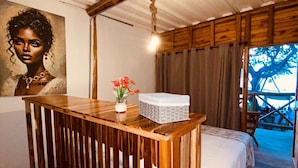 A rustic room with a wooden desk, a bed, a painting on the wall, and a view of the outdoors. - Rocha Beach Club (Cartagena)