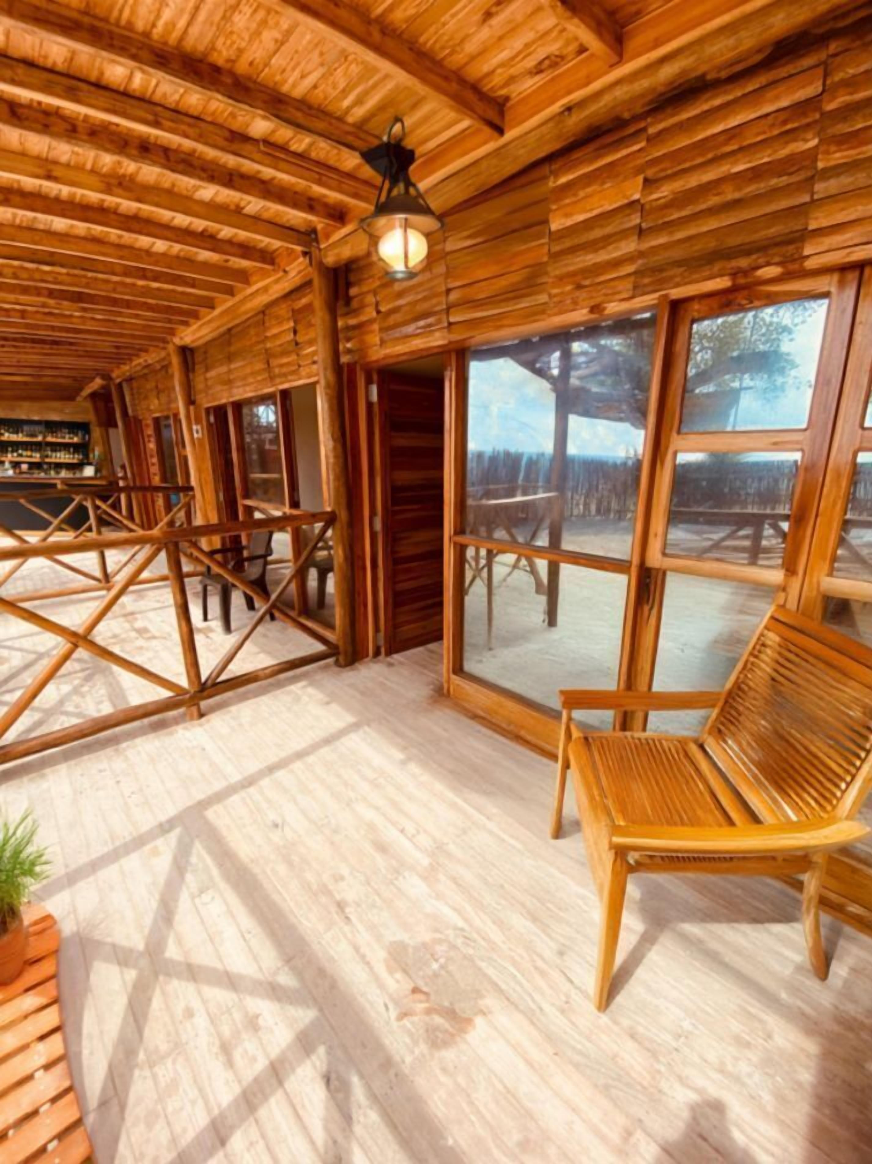 A wooden cabin interior with a large window, a wooden bench, and a hanging light fixture.