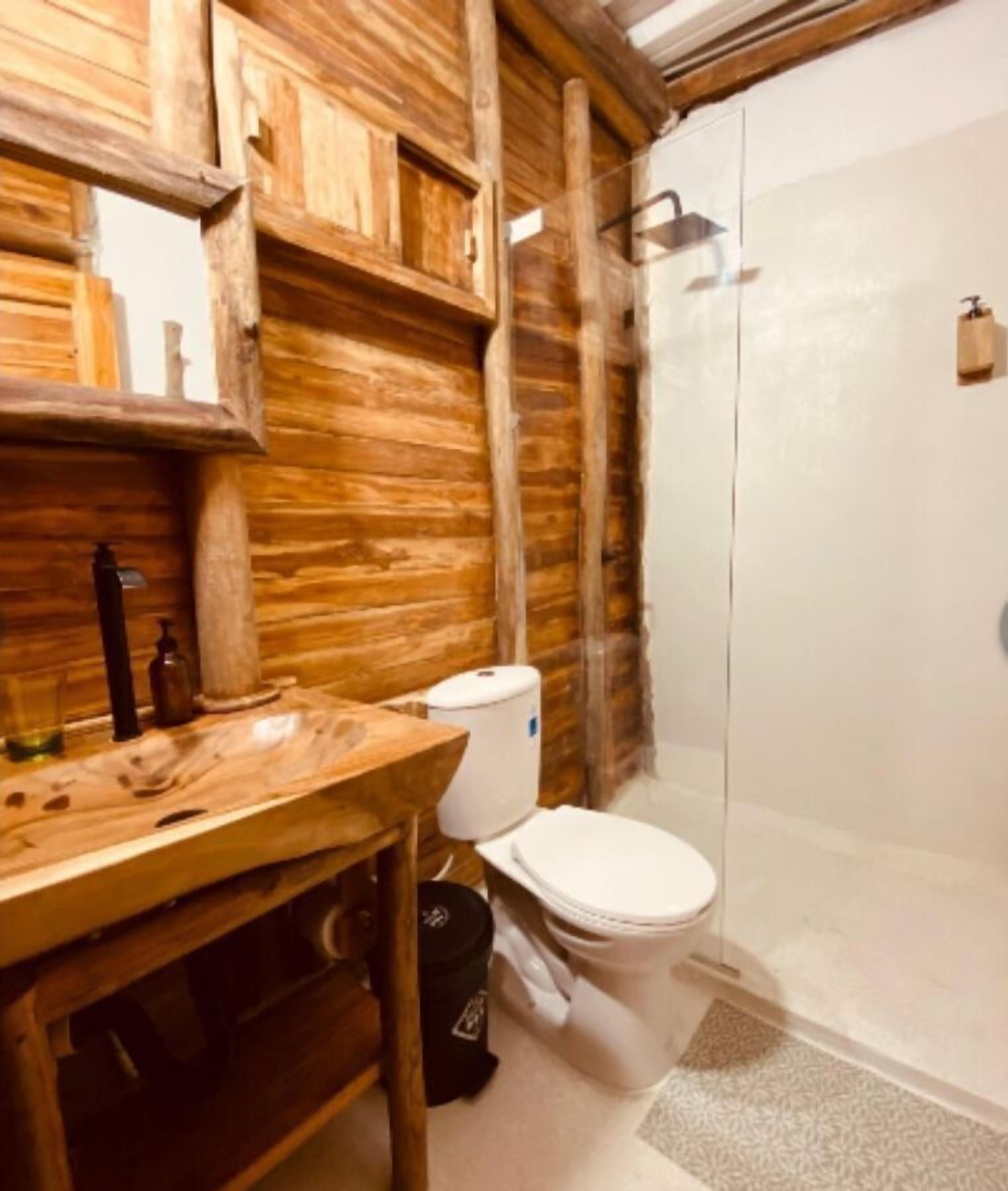 A bathroom with a wooden vanity, a toilet, and a shower enclosure.