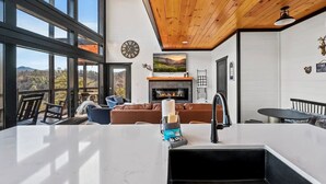 A modern kitchen with a large island, a fireplace, and a view of the outdoors. - Hill•of•a•View: Breathtaking Mountain Views & New Retreat (Sevierville)
