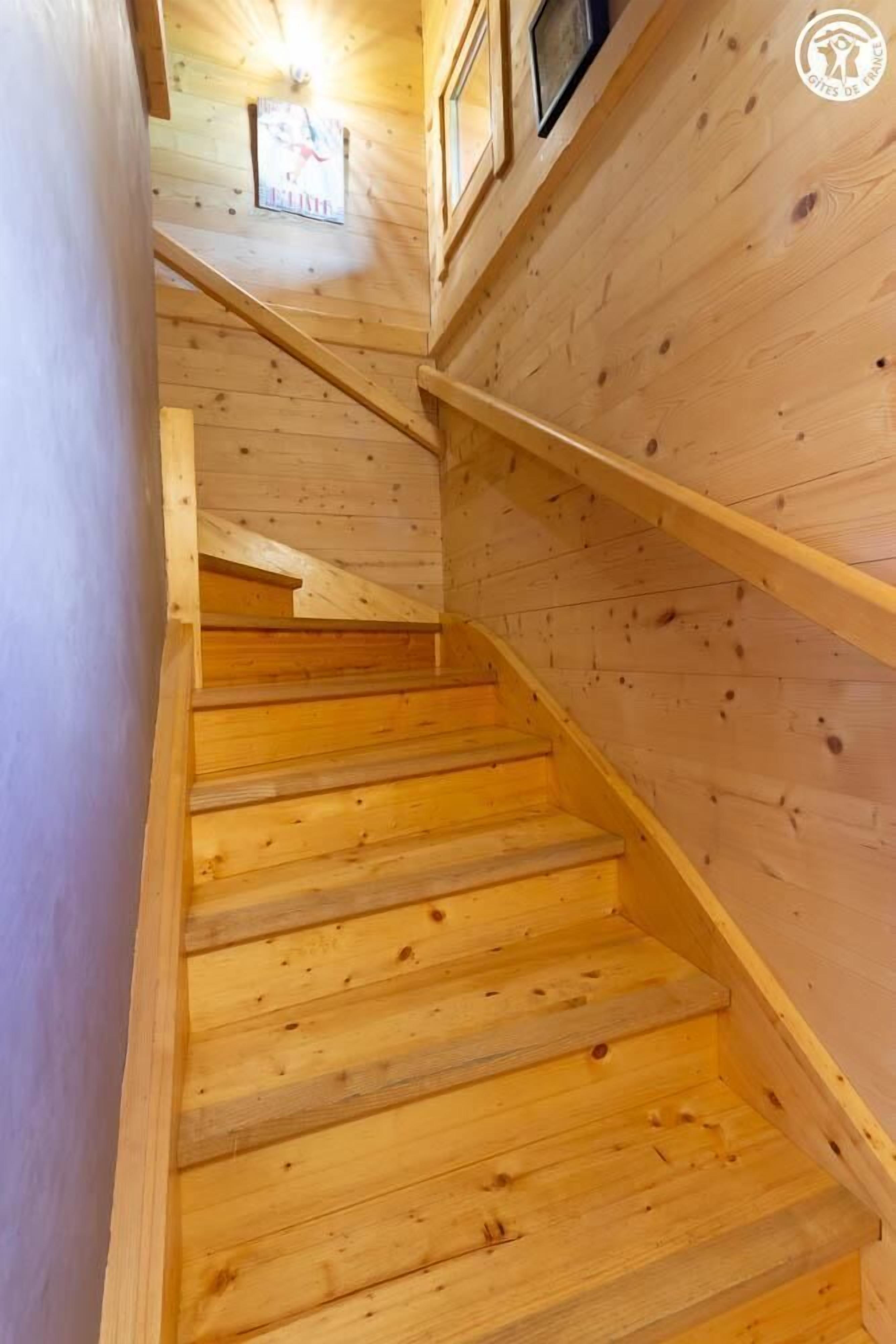 A wooden staircase with a handrail, leading to a landing with a framed picture and a small window.