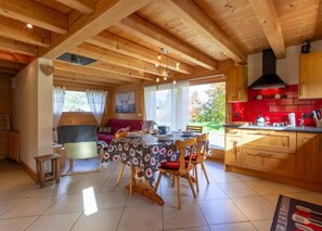 Cocina acogedora de estilo cabaña con vigas de madera, zona de comedor con una mesa dispuesta para cuatro personas y un reverso de azulejos rojos.