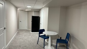 Un couloir avec une table ronde et deux chaises, un réfrigérateur et une porte.