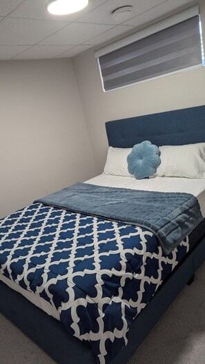 A neatly made bed with a blue and white patterned bedspread, a blue pillow, and a headboard. - One-BR Private Suite in South Winnipeg | Near UofM (STRA-2025-2655115) (Winnipeg)
